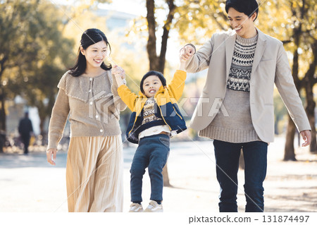 一個親密的家庭手牽手沿著秋天公園裡綠樹成蔭的小路散步 131874497