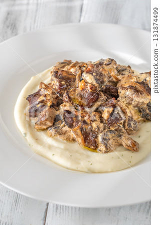Braised meat and mushroom topping over creamy mashed potato served on white plate 131874499