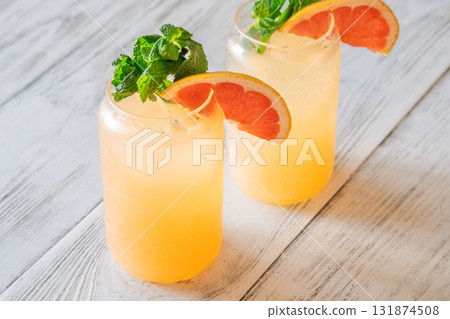 Two chilled Paloma cocktails with grapefruit slices and mint sprigs on white wood Two chilled Paloma cocktails with grapefruit slices and mint sprigs on white wood 131874508