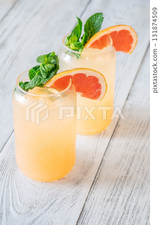 Two chilled Paloma cocktails with grapefruit slices and mint sprigs on white wood Two chilled Paloma cocktails with grapefruit slices and mint sprigs on white wood 131874509