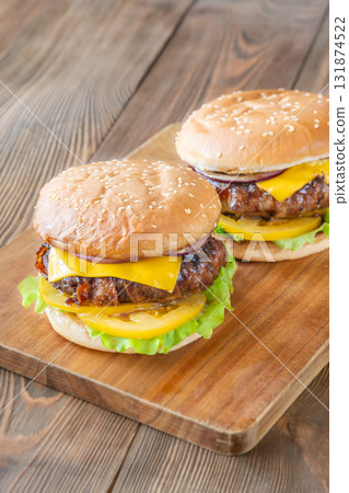 Two cheeseburgers with bacon and yellow tomato slices on rustic wooden board 131874522
