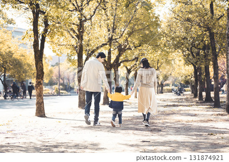 一個親密的家庭手牽手沿著秋天公園裡綠樹成蔭的小路散步 131874921