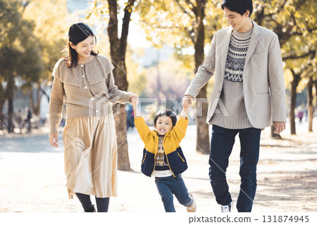 A close family walking hand in hand along a tree-lined path in an autumn park 131874945