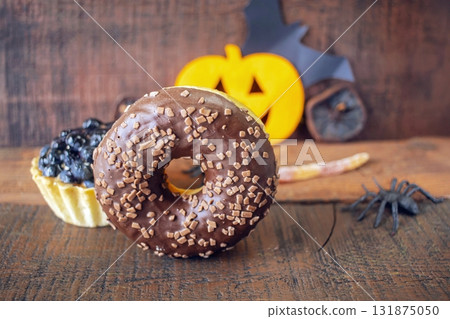 Spooky Halloween treats with blackberries and decorations on a wooden surface. Chocolate Halloween donut with spooky treats. 131875050