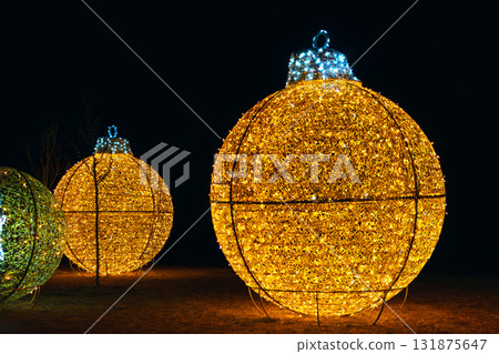 Giant golden installation, Christmas holiday ornament with festive lights glowing at night outdoors Giant golden installation, Christmas holiday ornament with festive lights glowing at night outdoors 131875647