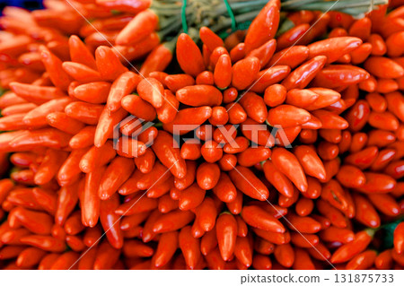 Fresh red chili peppers displayed in bunches at a market stall, symbolizing spicy food, organic 131875733