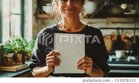 A Smiling Woman Holding a Blank Sheet of Paper in a Bright and Modern Kitchen, Showcasing Creativity and Happiness 131876133