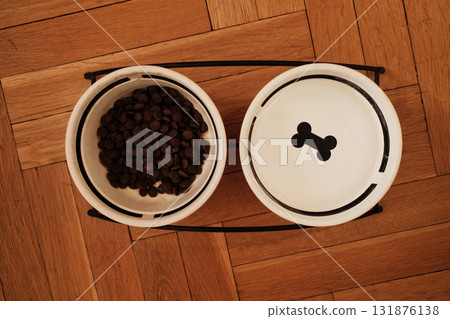 Two ceramic bowls for pet food and water on a wooden parquet floor, minimalist setup with warm indoor lighting. Pet care concept Two ceramic bowls for pet food and water on a wooden parquet floor, minimalist setup with warm indoor lighting. Pet care concept 131876138