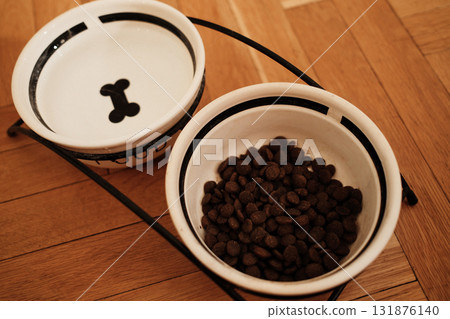 Two ceramic bowls for pet food and water on a wooden parquet floor, minimalist setup with warm indoor lighting. Pet care concept Two ceramic bowls for pet food and water on a wooden parquet floor, minimalist setup with warm indoor lighting. Pet care concept 131876140