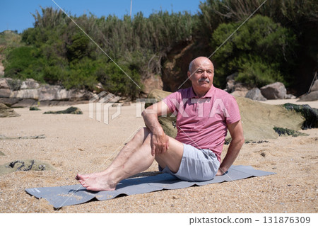 lderly man doing yoga twist pose sitting by the ocean shore lderly man doing yoga twist pose sitting by the ocean shore 131876309