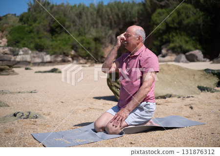 Elderly man practicing yoga breathing exercises, pranayama, sitting by the ocean shore Elderly man practicing yoga breathing exercises, pranayama, sitting by the ocean shore 131876312