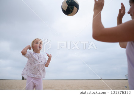 Mother teaching her 4-year-old daughter to play volleyball on the beach  131876353