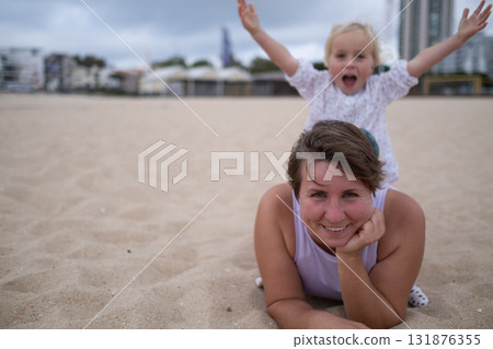 Woman in sportswear relaxing on the beach with her daughter on the sand.  131876355