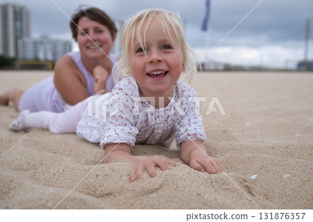 Woman in sportswear relaxing on the beach with her daughter on the sand.  131876357