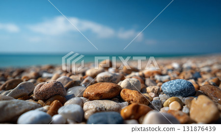 A low-angle, close-up shot of wet, multi-colored pebbles on a beach, stretching toward a blue sea and sky under bright sunlight. 131876439