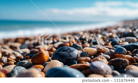 A low-angle, close-up shot of wet, multi-colored pebbles on a beach, stretching toward a blue sea and sky under bright sunlight. 131876440
