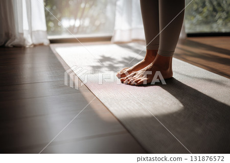 Partial view of bare feet on yoga mat in sunlit room, soft morning light creates peaceful and calm atmosphere, indoor wellness and mindfulness practice 131876572