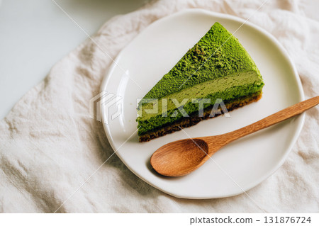 Slice of matcha cake on white ceramic plate with wooden spoon, green tea dessert, minimal style, soft natural light, elegant presentation, sweet treat, cozy atmosphere Slice of matcha cake on white ceramic plate with wooden spoon, green tea dessert, minimal style, soft natural light, elegant presentation, sweet treat, cozy atmosphere 131876724