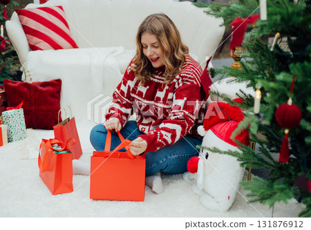 Middle age Caucasian woman smiling confident holding Christmas gift bag at home. Winter time and holidays. Celebration banner, big sale concept 131876912