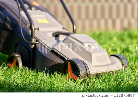 Electric lawn mower cutting green grass in backyard 131876997