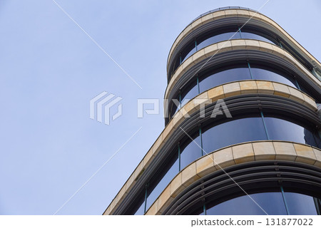 Modern glass building with curved facade against blue sky Modern glass building with curved facade against blue sky 131877022