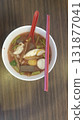 Spicy pink soup with fish balls, tofu and greens in white bowl with chopsticks and spoon, comforting street food meal, savory and vibrant 131877041