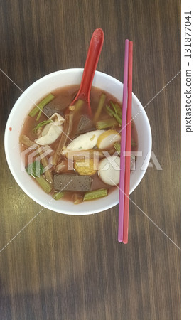Spicy pink soup with fish balls, tofu and greens in white bowl with chopsticks and spoon, comforting street food meal, savory and vibrant Spicy pink soup with fish balls, tofu and greens in white bowl with chopsticks and spoon, comforting street food meal, savory and vibrant 131877041