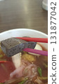 Dark tofu cube held with red chopstick above clear noodle soup with greens and broth 131877042