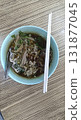 Shredded beef noodle soup in ceramic bowl with chopsticks and spoon, savory broth and fresh herbs, comforting street food meal 131877045