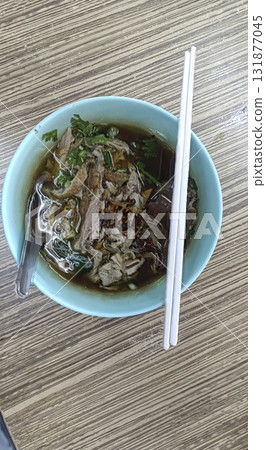 Shredded beef noodle soup in ceramic bowl with chopsticks and spoon, savory broth and fresh herbs, comforting street food meal Shredded beef noodle soup in ceramic bowl with chopsticks and spoon, savory broth and fresh herbs, comforting street food meal 131877045