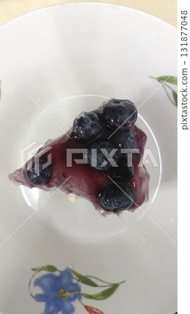 Blueberry topping cheesecake slice white plate with floral pattern, glossy fruit glaze and creamy texture, appetizing dessert presentation Blueberry topping cheesecake slice white plate with floral pattern, glossy fruit glaze and creamy texture, appetizing dessert presentation 131877048
