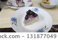 Blueberry cheesecake slice with glossy fruit topping and creamy filling on floral porcelain plate, inviting dessert scene with soft lighting 131877049