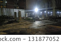 Construction site at night illuminated by bright floodlight and scattered building materials, concrete columns and temporary fencing 131877052