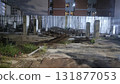 Abandoned construction site at night with corrugated metal fence, concrete pillars, scattered rebar and debris under moody lighting 131877053