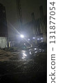 Dimly lit construction site at night with wet reflective ground and bright floodlight creating moody atmosphere 131877054