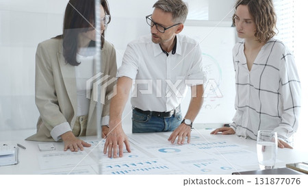 Professional team analyzing financial charts, colleagues reviewing data with focused expressions in modern workplace setting. Business people concept 131877076