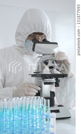 A medical virologist in protective gear examines viral samples under a microscope while conducting research in a laboratory setting A medical virologist in protective gear examines viral samples under a microscope while conducting research in a laboratory setting 131877093