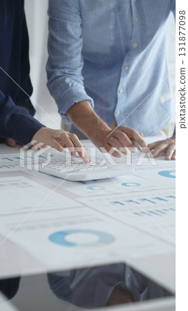 Professional team collaborating, reviewing financial graphs, calculating metrics, discussing performance insights and strategic planning in modern corporate workspace. Business people concept 131877098