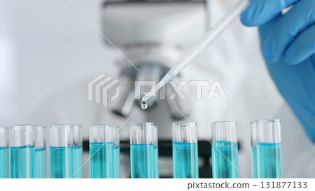 Close up of scientific researcher wearing protective gear, carefully pipetting liquid into test tubes while conducting medical research experiment in laboratory. Medicine, healthcare and science 131877133