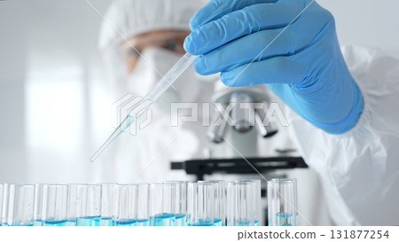Scientific researcher wearing protective equipment, carefully pipetting liquid into test tubes while conducting medical research experiment. Medicine, healthcare and science concept 131877254
