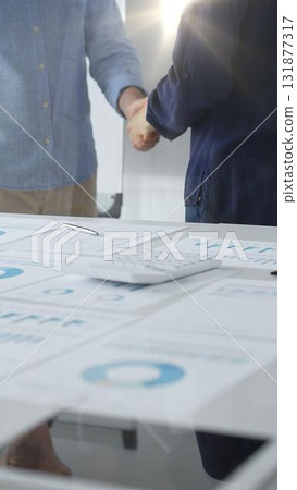 Business partners shaking hands after successful agreement over financial documents, calculator and pen on white table in office. Handshake concept 131877317