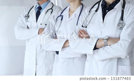 Medics from the team in white coats and with stethoscopes stand with their arms folded across their chests, embodying cohesion, professional success, and trust in the healthcare sector 131877483