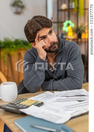 Indian man bends forward head in hands unpaid bills on table calculator and laptop heavy worry money 131877770