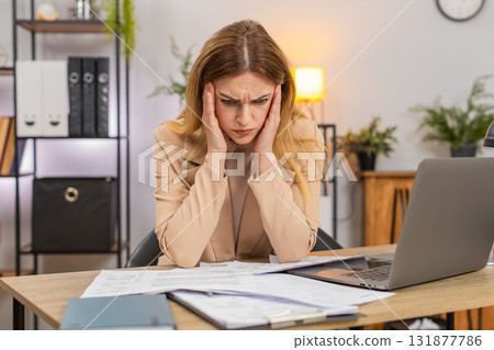 Businesswoman faces pile of bills sees costs up unhappy confused plans savings prints plan on laptop 131877786