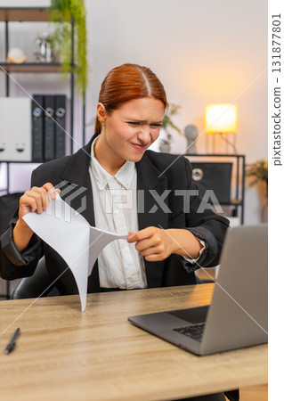 Young businesswoman tears draft report after error then opens new document typing eagerly on laptop Young businesswoman tears draft report after error then opens new document typing eagerly on laptop 131877801