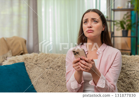 Young woman frowning at smartphone after contest loss shows sad reaction and very strong frustration 131877830