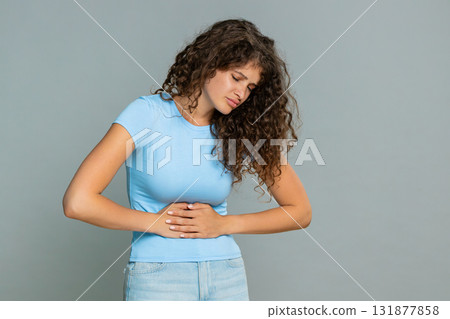 Woman suffering sharp stomach pain holding abdomen bending forward discomfort unhealthy reaction Woman suffering sharp stomach pain holding abdomen bending forward discomfort unhealthy reaction 131877858
