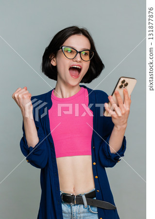 Woman looking at smartphone smiling joyfully raising hand celebrating online victory lottery win Woman looking at smartphone smiling joyfully raising hand celebrating online victory lottery win 131877876