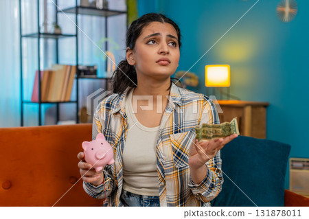 Woman sadly looking at piggy bank with one dollar inside financial difficulties limited savings Woman sadly looking at piggy bank with one dollar inside financial difficulties limited savings 131878011