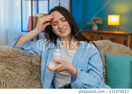 Woman suffering severe headache sitting holding head exhausted searching taking pain relief pills Woman suffering severe headache sitting holding head exhausted searching taking pain relief pills 131878013
